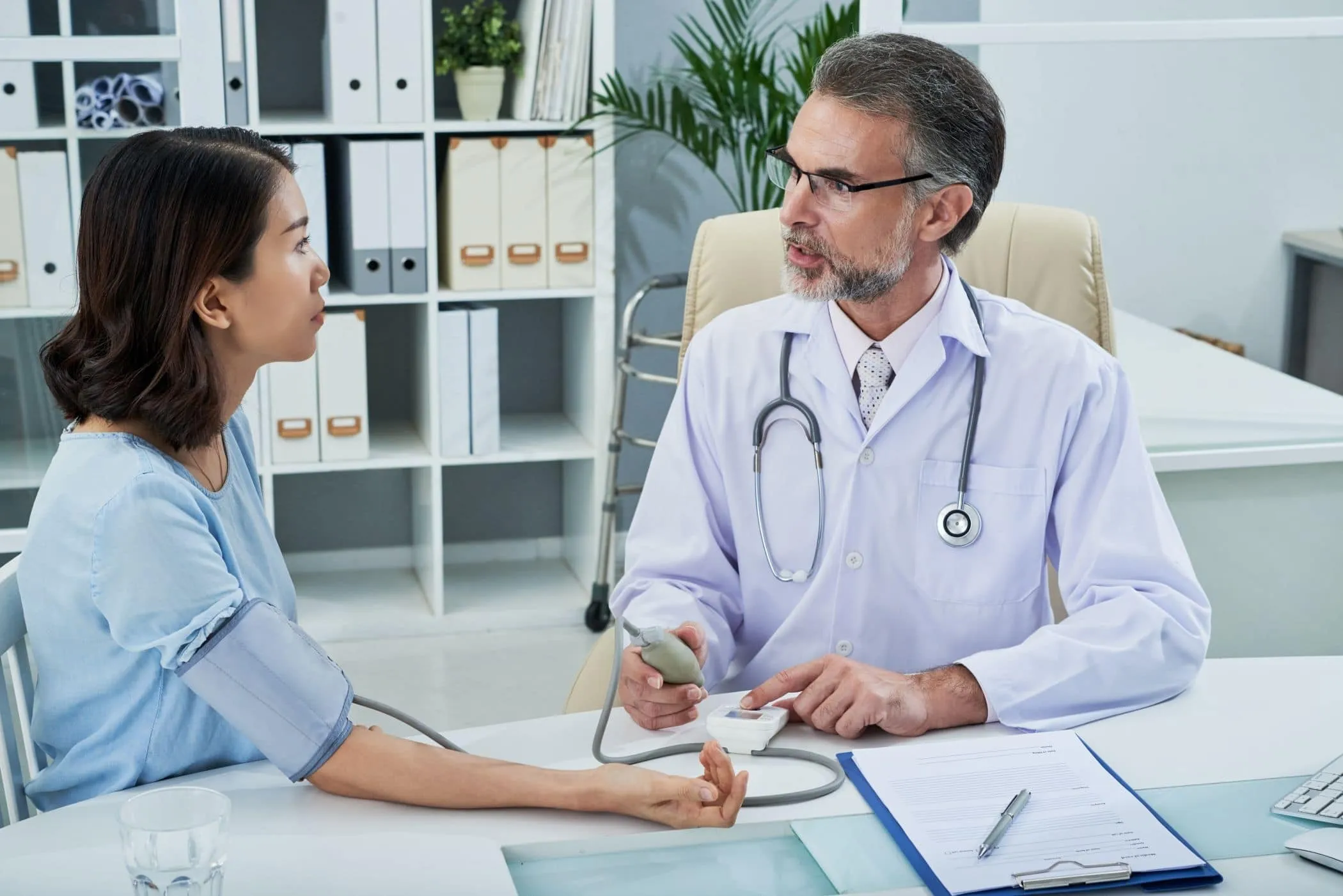 A doctor taking a patient's blood pressure across his desk