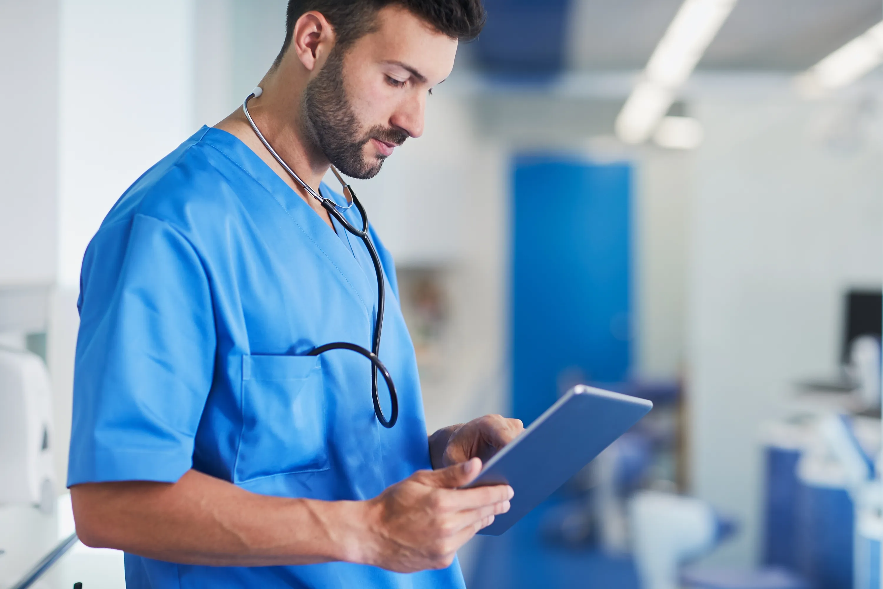 A clinician in blue scrubs checking a tablet