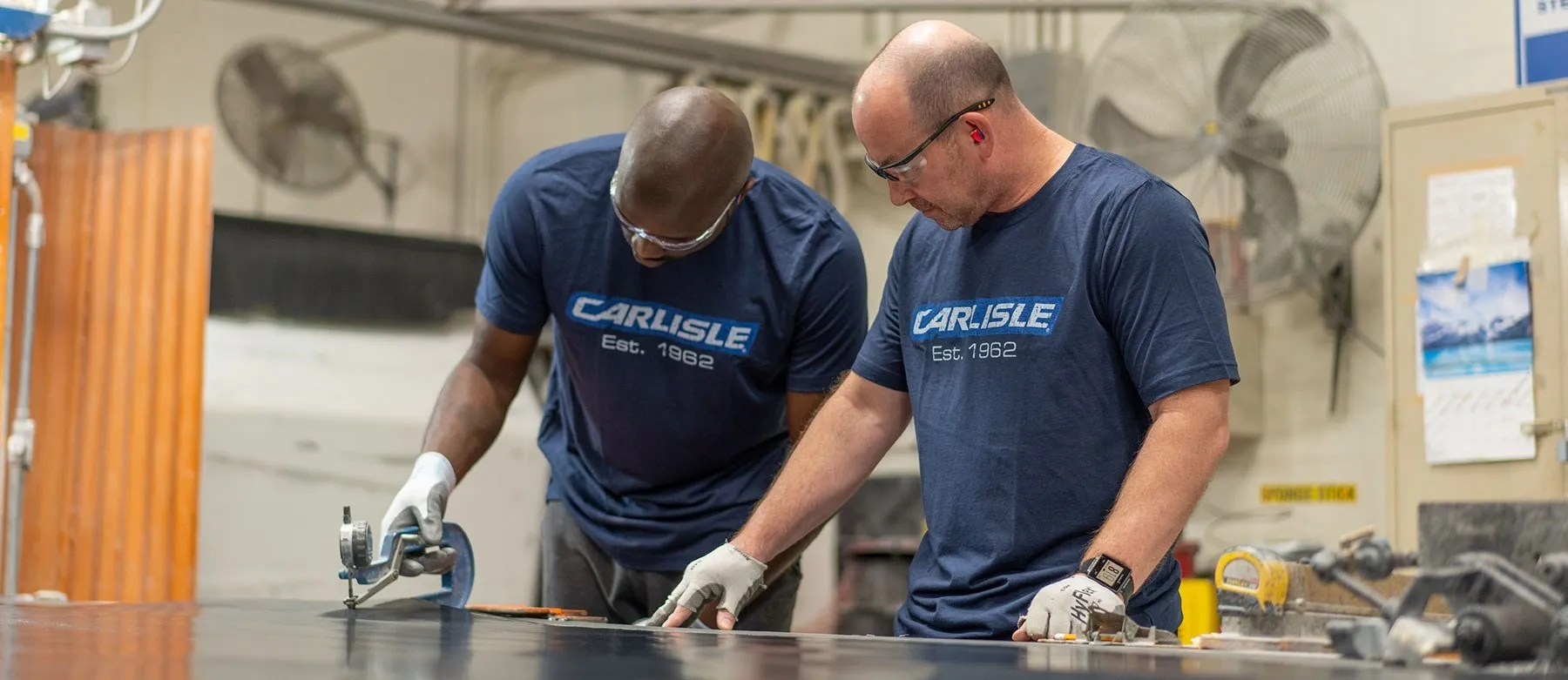 Two Carlisle workers cutting material at a shop workbench