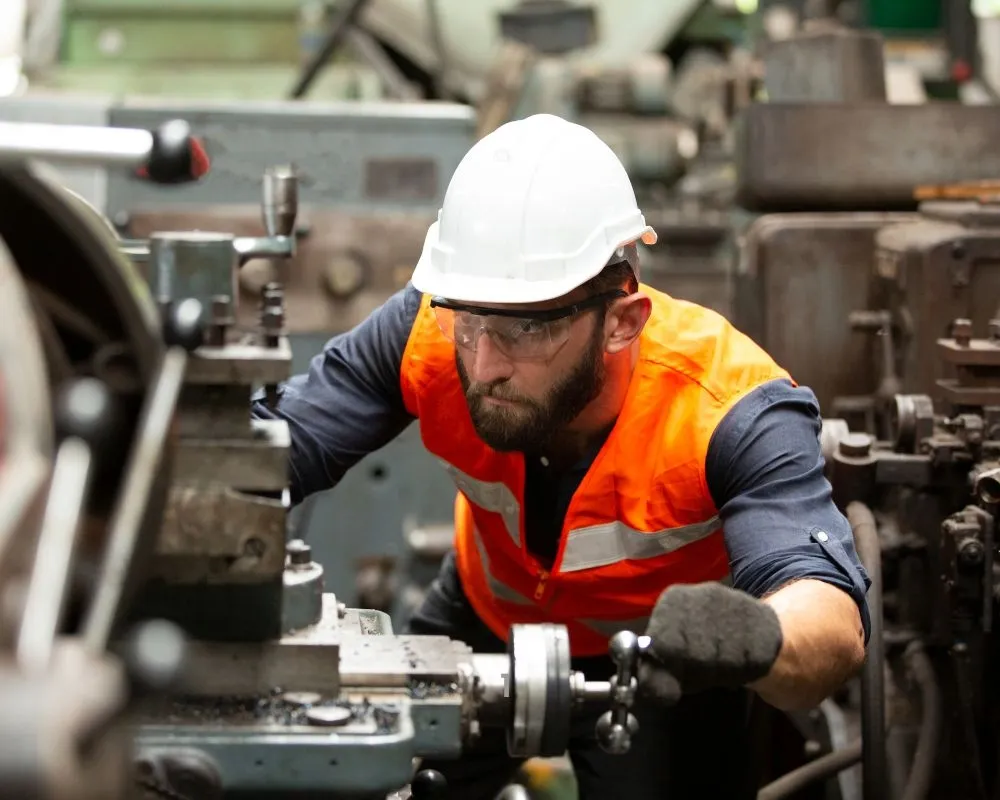 A machinist in a hard hat and safety vest operating an industrial lathe