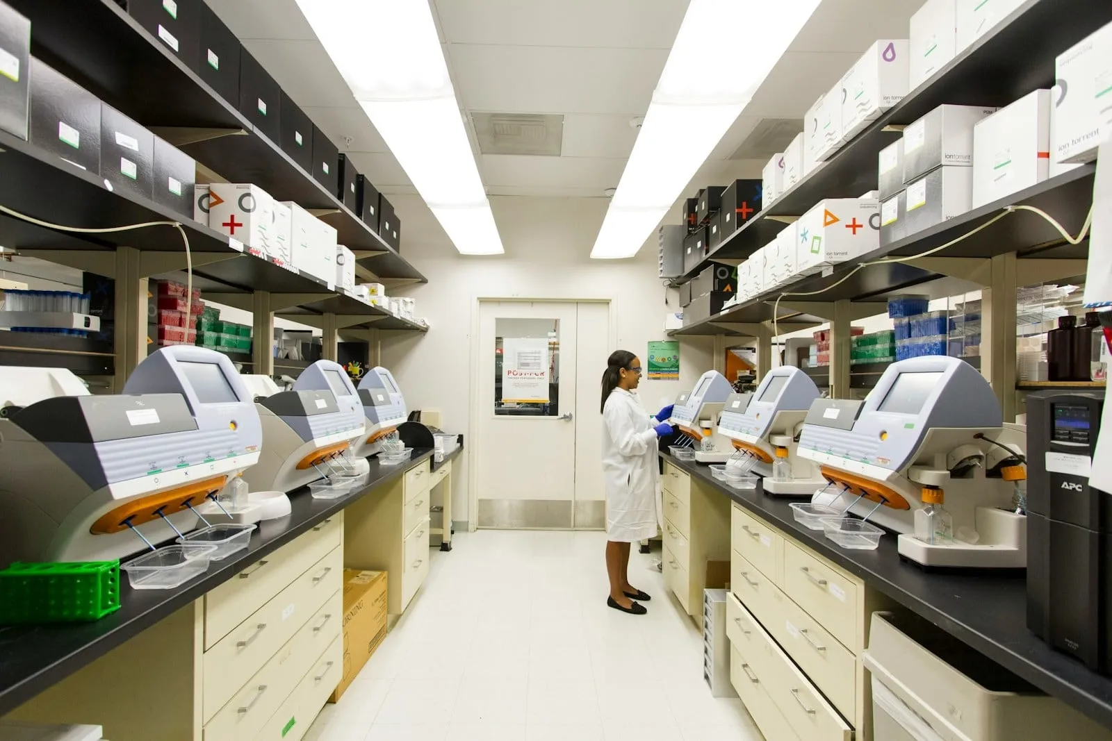 A pharmacy lab with automated dispensing machines along both counters and a technician at work