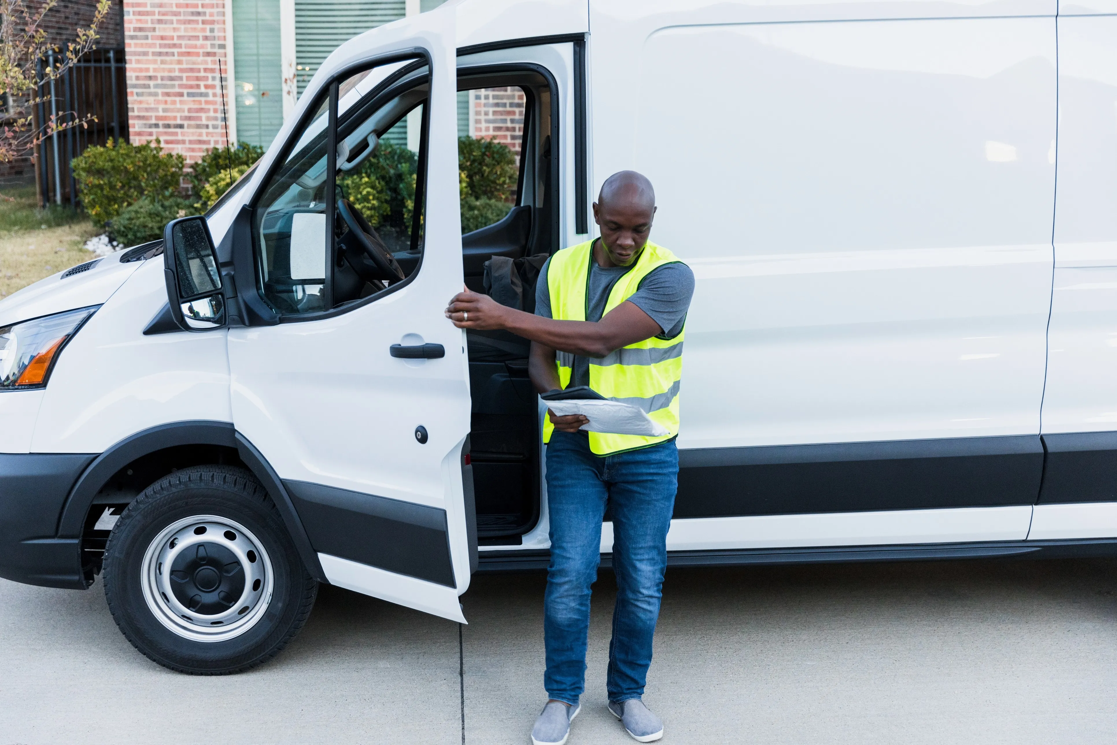 A field technician in a safety vest checking paperwork beside a white van