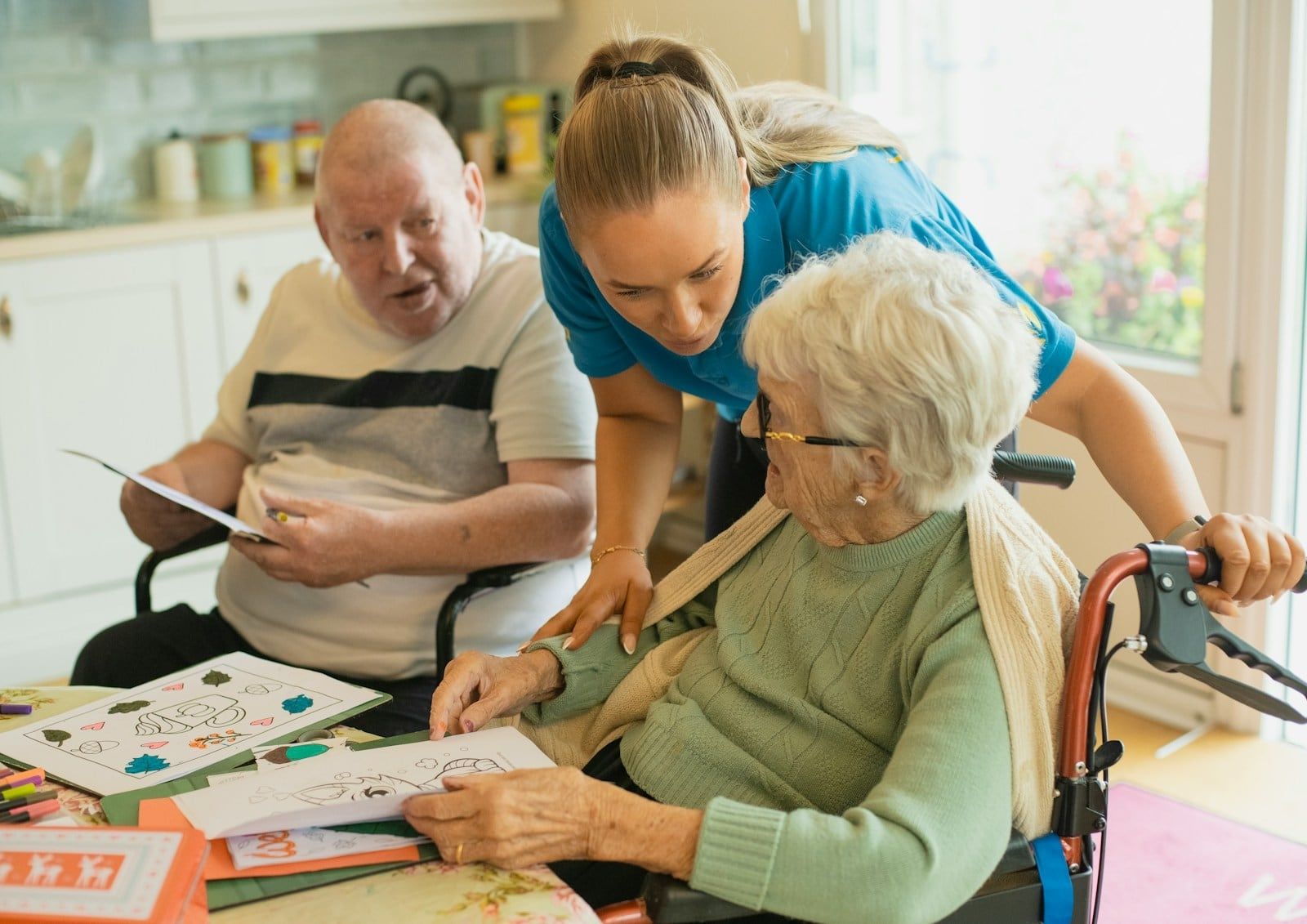 A caregiver helping two older adults with an activity at a table