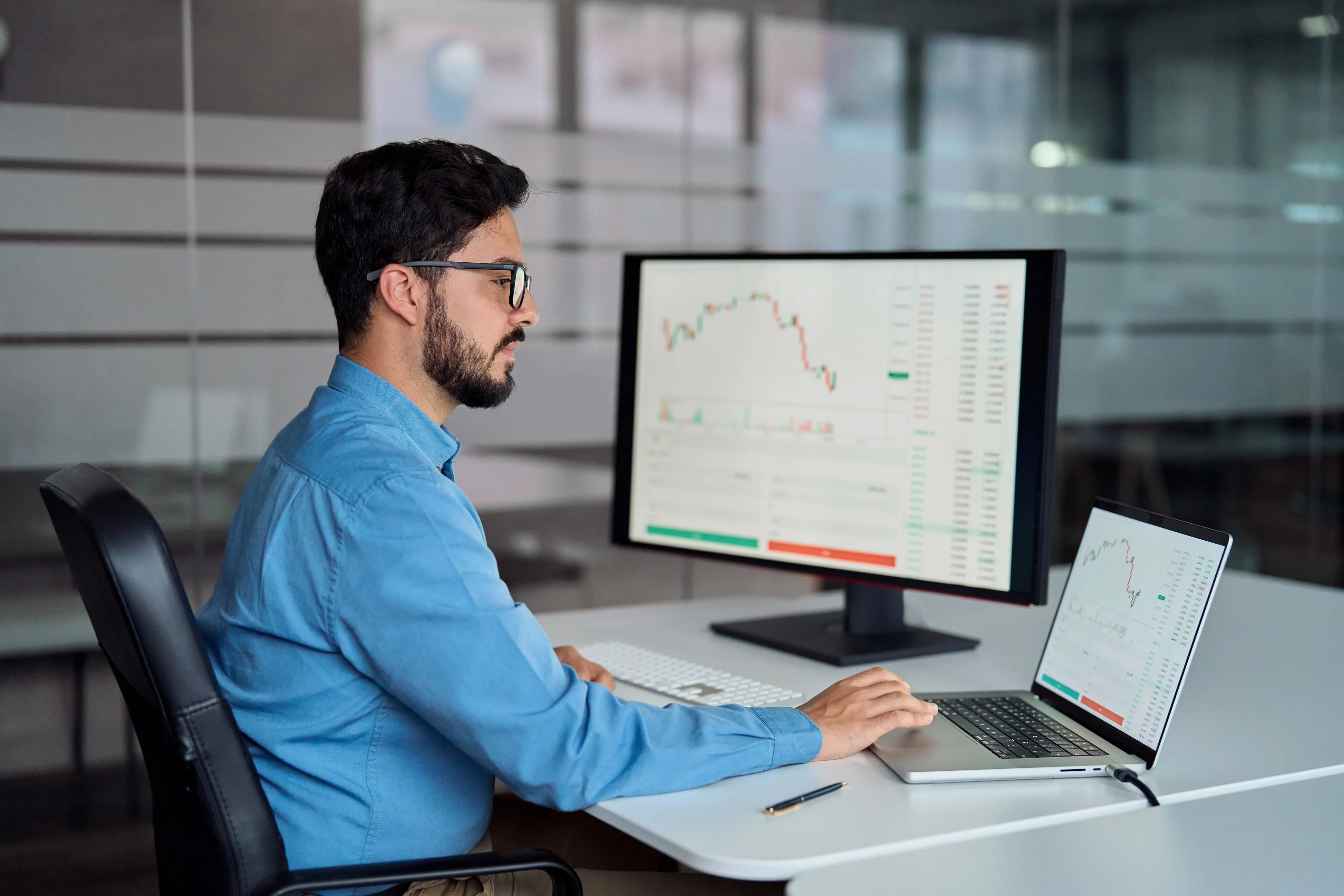 An analyst at a desk reviewing financial charts on two screens
