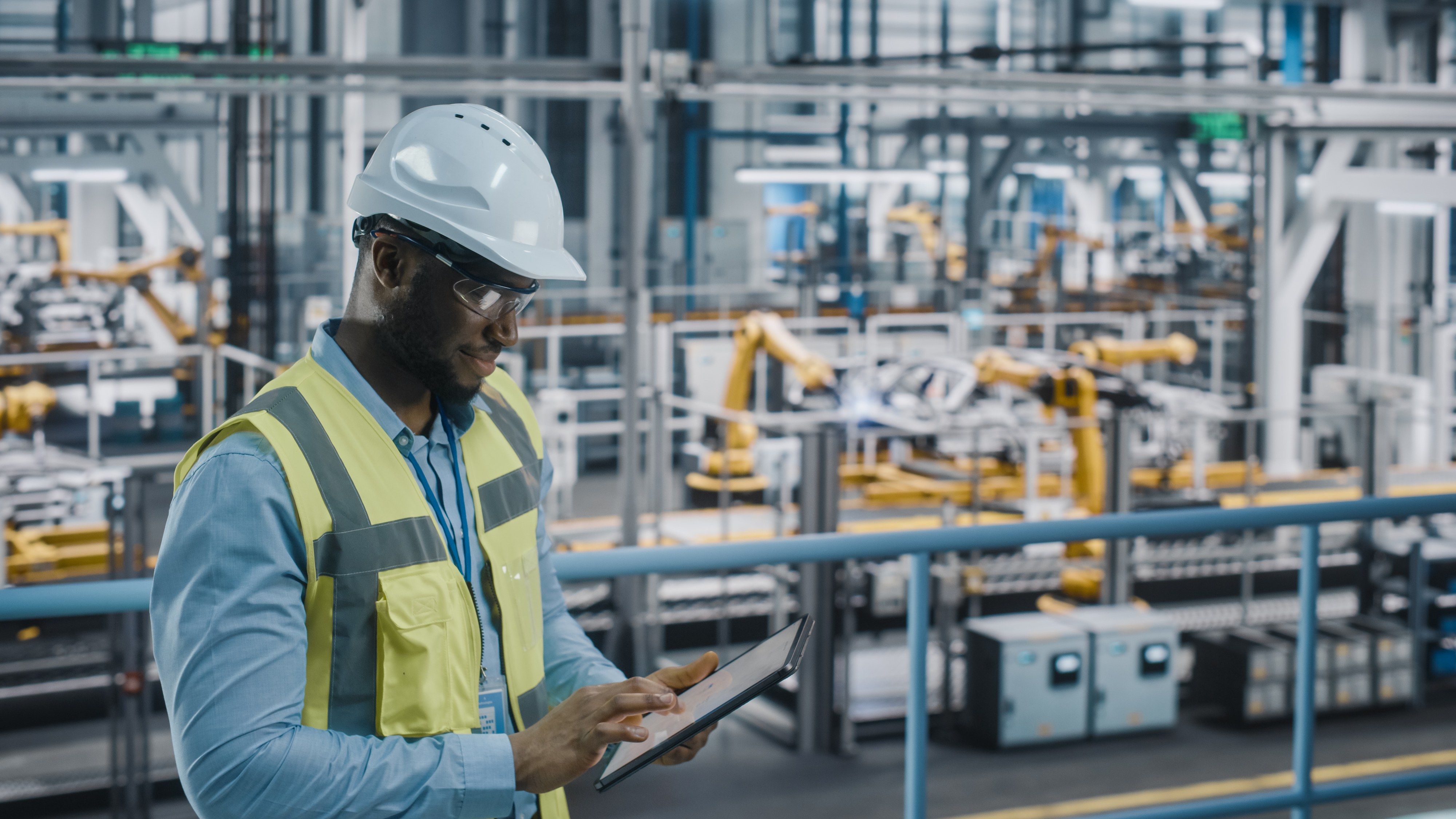 A worker in a hard hat and safety vest checking a tablet on a factory floor
