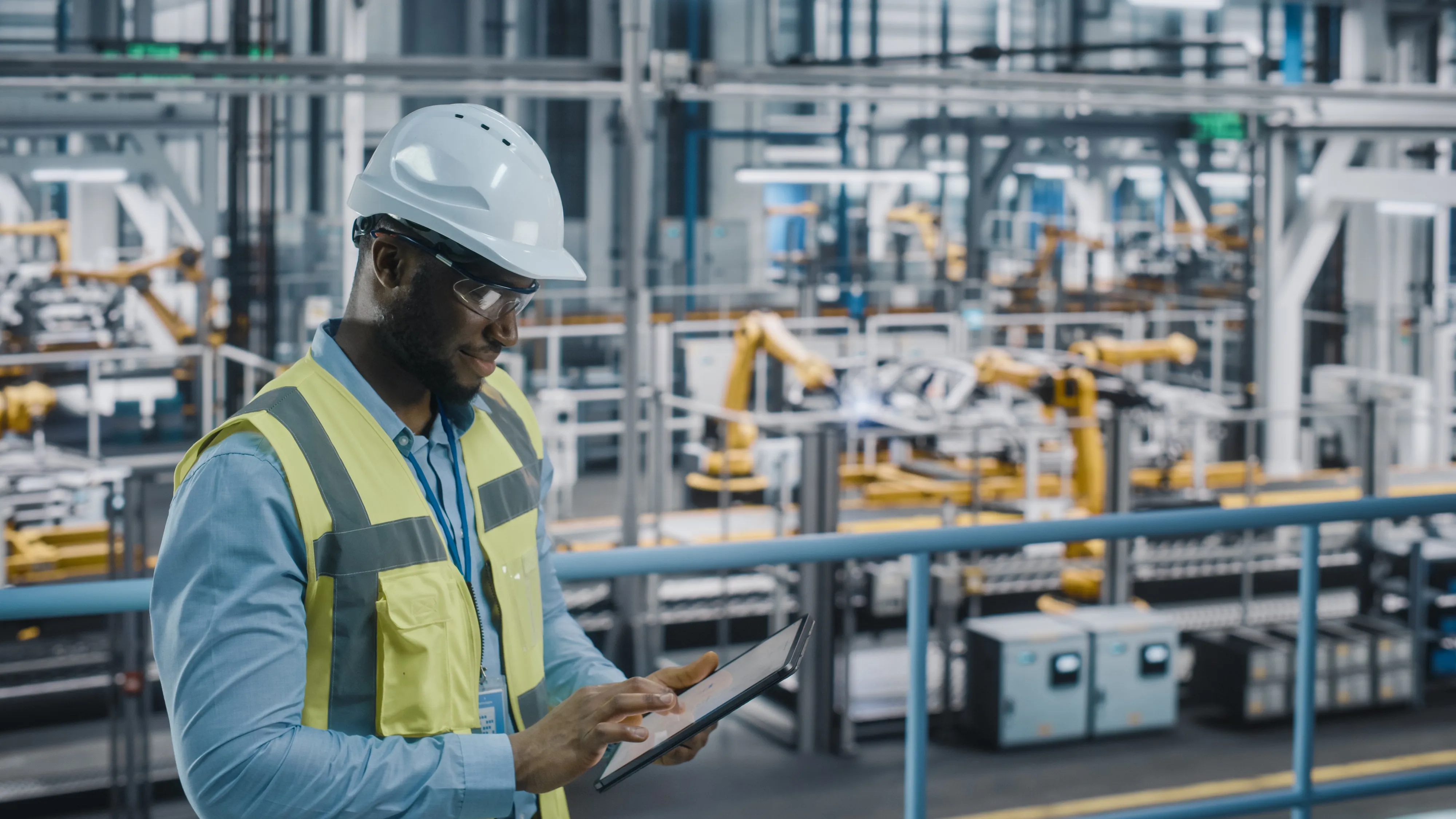 A worker in a hard hat and safety vest checking a tablet on a factory floor