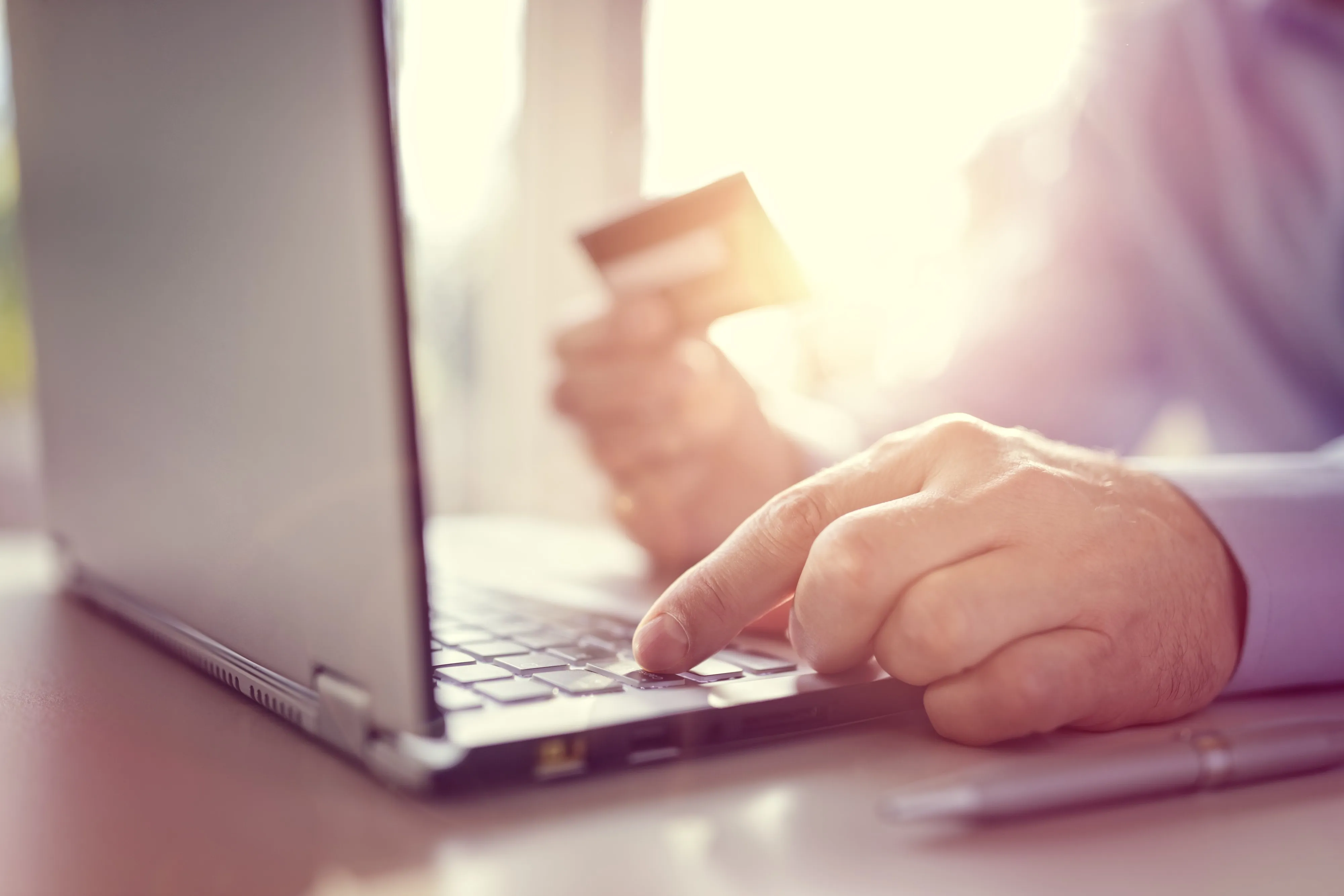 A hand holding a payment card while typing on a laptop