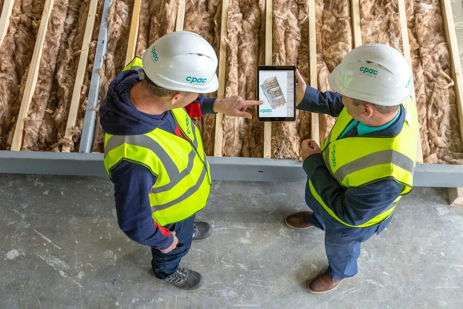 Two builders in hard hats reviewing a tablet on a construction site