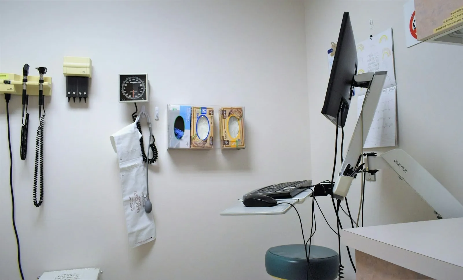 An empty exam room with a wall-mounted computer and diagnostic instruments