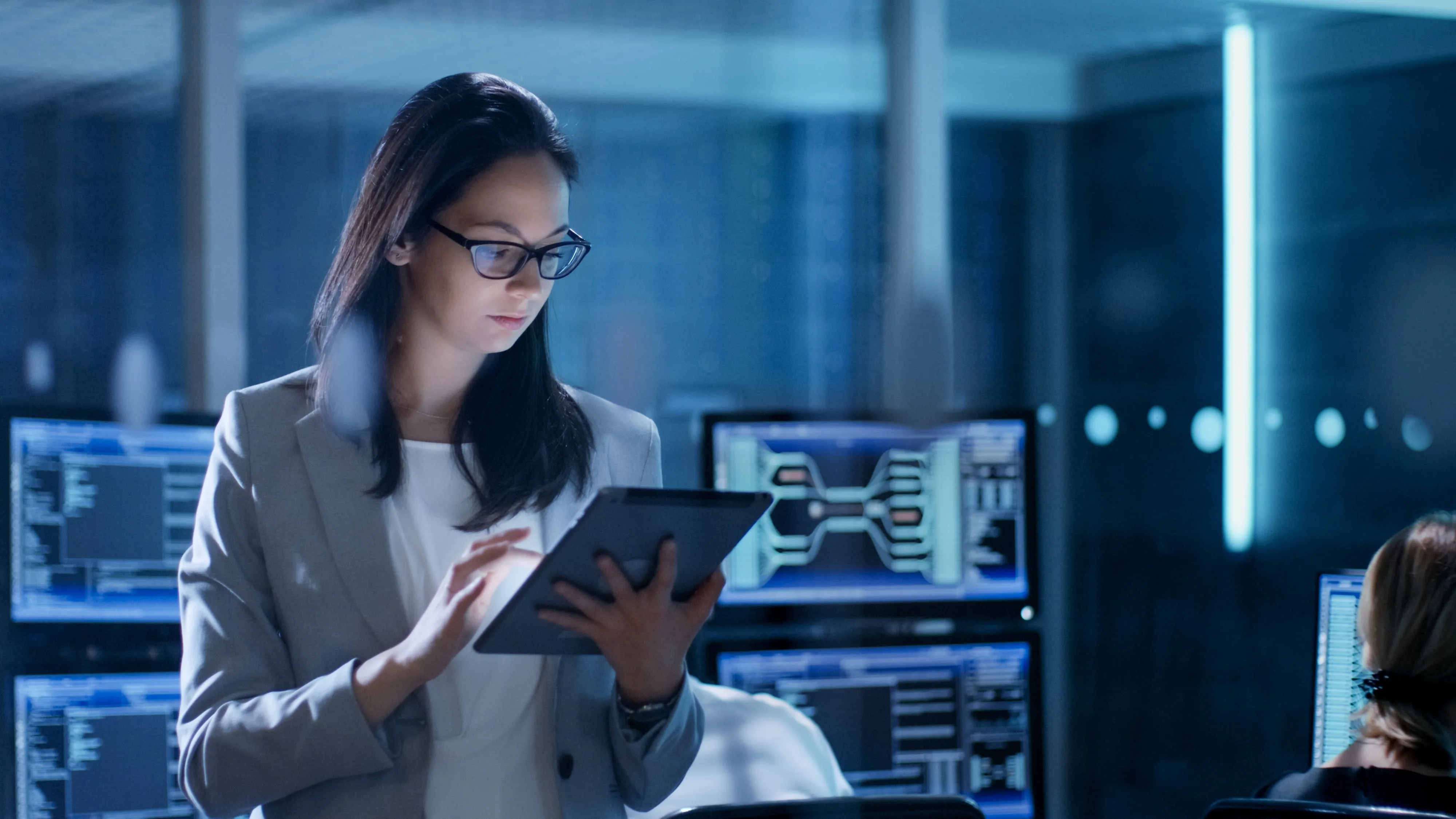 A woman using a tablet in a room full of monitoring screens